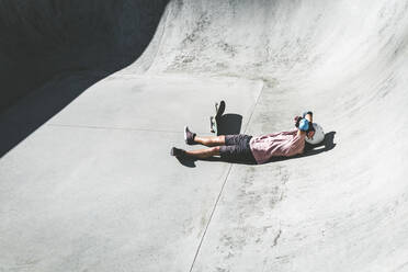 Männlicher Sportler, der sich an einem sonnigen Tag im Skateboard-Park entspannt - OMIF00053