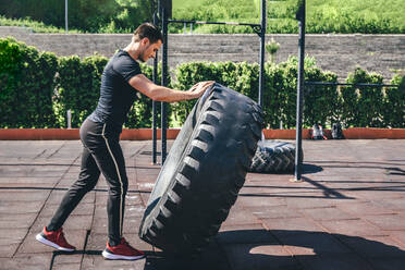 Männlicher Sportler beim Training mit einem großen Reifen an einem sonnigen Tag - OMIF00062