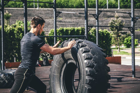 Sportler beim Training mit schweren Reifen an einem sonnigen Tag - OMIF00064