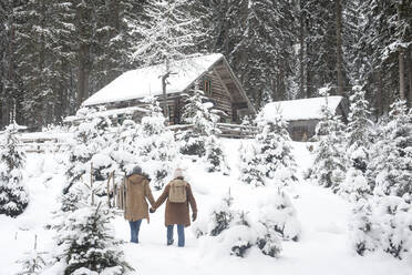 Junges Paar hält sich an den Händen, während es im Schnee spazieren geht - HHF05684