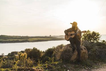 Mann mit Hut spielt Gitarre und sitzt auf einem Felsen - AFVF09208