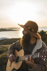 Mann mit Bart spielt Gitarre bei Sonnenuntergang - AFVF09209