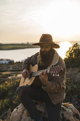 Junger Mann spielt Gitarre und sitzt auf einem Felsen - AFVF09210