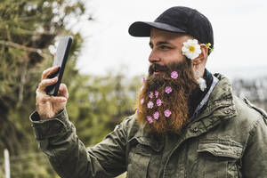 Hipster-Mann mit Blumen im Bart nimmt Selfie durch Smartphone - AFVF09214