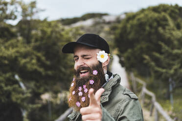 Glücklicher junger Mann mit Blumen, der mit den Augen zwinkert - AFVF09220