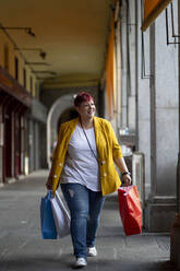 Smiling woman with shopping bags walking at corridor - OCMF02235