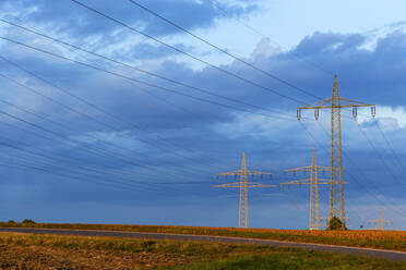 Electricity pylons standing against blue cloudy sky - NDF01342