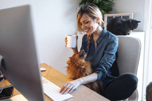 Lächelnde Influencerin betrachtet ihren Hund beim Kaffee zu Hause - JSRF01627