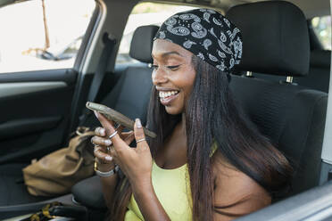 Glückliche Frau, die im Auto sitzend eine Sprachnachricht über ihr Mobiltelefon verschickt - JRVF01794