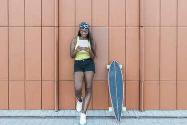 Frau, die ein digitales Tablet benutzt, während sie auf dem Gehweg neben einem Skateboard steht - JRVF01809