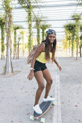 Frau mit Rucksack, die auf dem Gehweg Skateboard fährt - JRVF01815