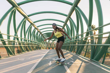 Lächelnde mittelgroße erwachsene Frau, die auf einer Brücke Skateboard fährt - JRVF01822