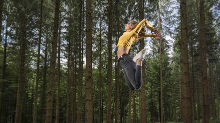 Carefree sportswoman jumping in forest - STSF03039