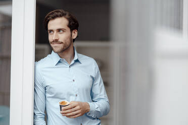 Businessman with disposable coffee cup leaning on door - KNSF08935