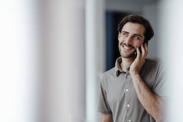 Smiling man talking on mobile phone at home - KNSF08965