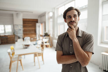 Thoughtful man with hand on chin standing at home - KNSF08967