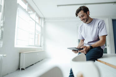 Happy man using digital tablet while sitting on table - KNSF08973