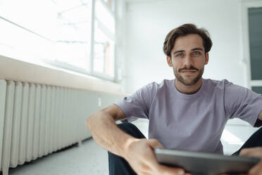 Lächelnder Mann mit digitalem Tablet, der zu Hause sitzt - KNSF08975