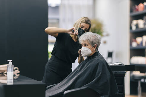 Friseurin beim Haareschneiden eines Kunden im Salon während COVID-19 - OCAF00764