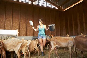 Female farmer walking amidst goats at farm - VEGF04992