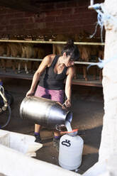 Bäuerin gießt Milch in einen Behälter auf dem Bauernhof - VEGF04998