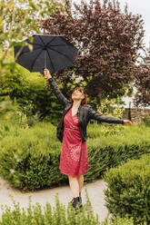 Frau mit Regenschirm genießt regnerischen Tag im Park - MGRF00495