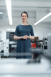 Female professional with hands clasped standing in workshop - KNSF08983