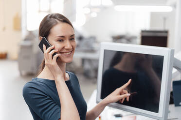 Geschäftsfrau, die auf den Bildschirm zeigt, während sie mit einem Mobiltelefon in der Industrie spricht - KNSF08984