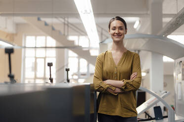 Smiling businesswoman standing with arms crossed in workshop - KNSF08989