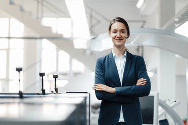 Confident businesswoman standing with arms crossed in industry - KNSF09002