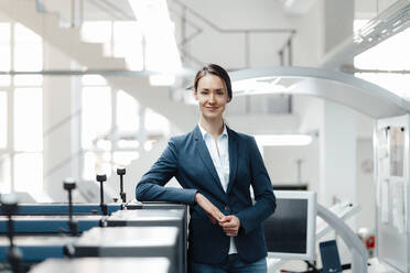 Female professional leaning on machine in workshop - KNSF09004