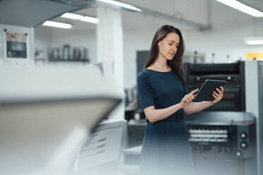 Weibliche Fachkraft, die ein digitales Tablet benutzt, während sie in einer Werkstatt steht - KNSF09014