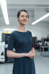 Smiling businesswoman with hands clasped standing in industry - KNSF09032