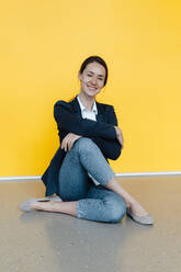 Smiling businesswoman with arms crossed practicing yoga on floor - KNSF09039