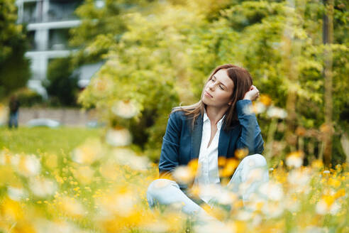 Junge Geschäftsfrau mit braunem Haar sitzt im Park - GUSF06467