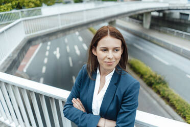 Confident businesswoman standing with arms crossed leaning on railing at bridge - GUSF06487