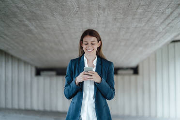 Smiling female freelancer surfing net through smart phone in basement - GUSF06492