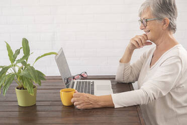 Smiling senior businesswoman having coffee during video conference at home - SIPF02366