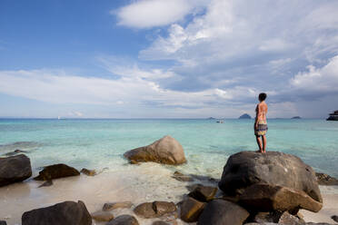 Rückansicht des ganzen Körpers von barfuß weiblichen Touristen in Badebekleidung stehen auf Felsen und bewundern azurblauen Meer während des Urlaubs in Malaysia - ADSF30314