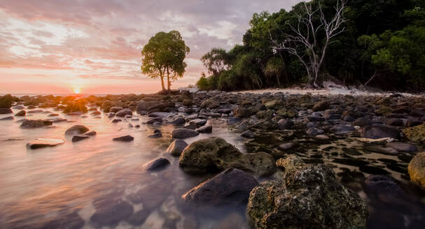 Landschaft mit nassen Felsbrocken, die von transparentem Meerwasser umspült werden, am Ufer mit tropischen Pflanzen bei Sonnenuntergang in Malaysia - ADSF30319