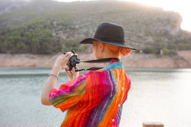 Frau mit schwarzem Hut in einem See, die die Landschaft fotografiert - ADSF30334