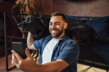 Glücklicher Mann macht Selfie mit Labrador Retriever im Wohnzimmer - VPIF04898