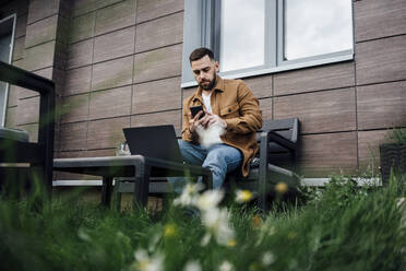 Male freelancer working on mobile phone in backyard - VPIF04900