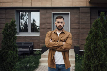 Confident man standing with arms crossed at backyard - VPIF04913