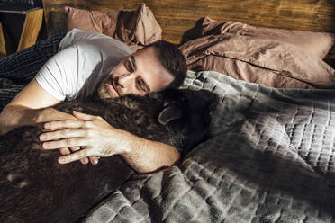 Mid adult man hugging dog on bed - VPIF04924