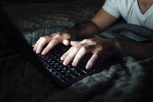 Mid adult man typing on laptop in dark room - VPIF04934