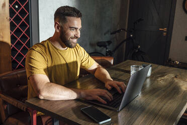 Lächelnder männlicher Freiberufler bei der Arbeit am Laptop im Home Office - VPIF04938