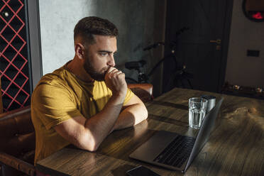 Nachdenklicher Geschäftsmann mit Laptop am Schreibtisch im Heimbüro - VPIF04939