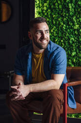 Smiling man with hands clasped on chair at home - VPIF04964