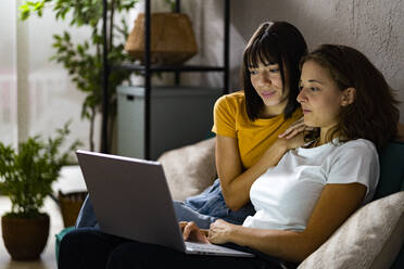 Lesbisches Paar benutzt einen Laptop, während es zu Hause auf dem Sofa sitzt - GIOF13508